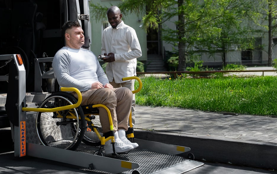 A man in a wheelchair boarding a transport van with a rear lift.