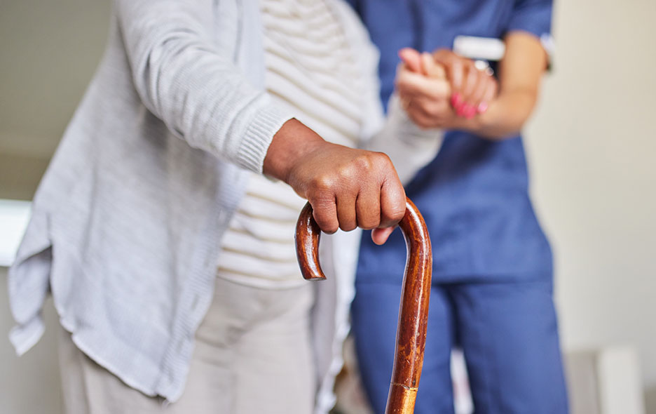 Patient using a cane with assistance from caregiver